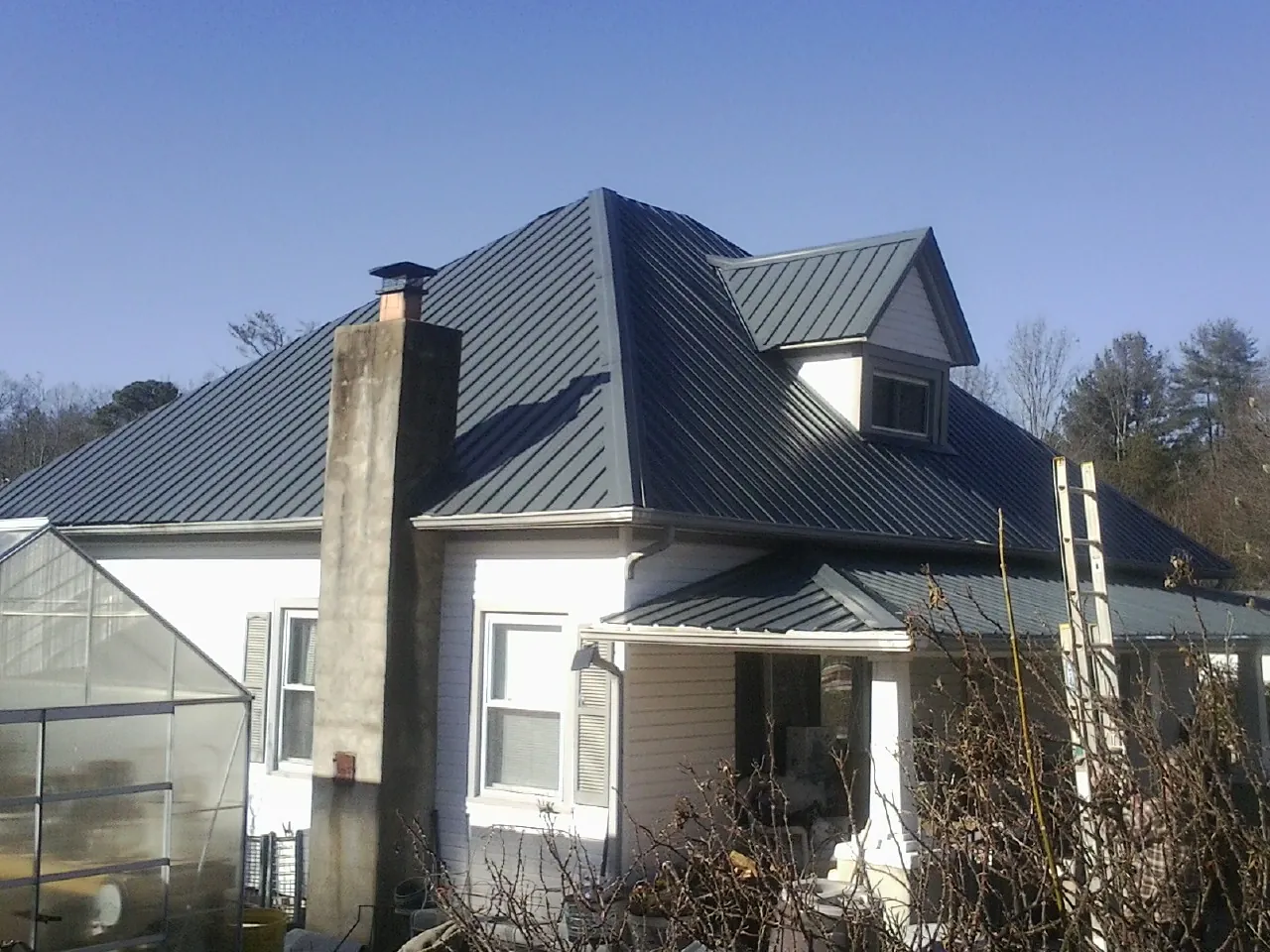 Dark blue standing seam metal roof on a white farmhouse with dormer — Slate & Tile Roof Repair by Roofing Brothers in Shady Cove