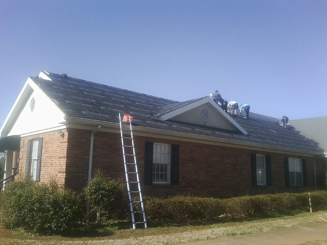 Crew tearing shingles off a brick ranch roof with a ladder set — Metal Roof Repair work by our crew in Shady Cove
