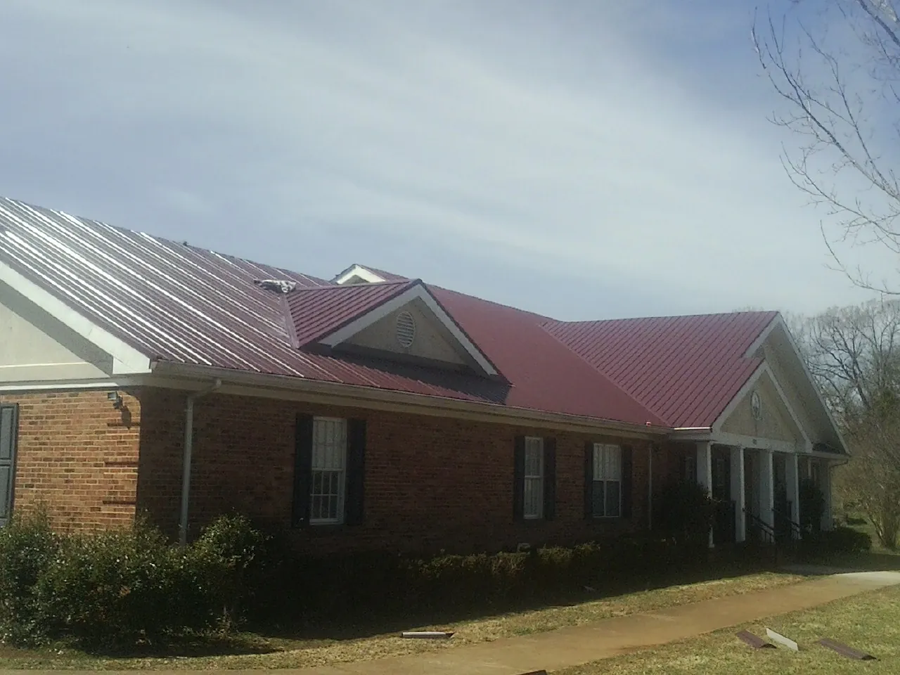 Red metal roof with gabled entries on a long brick building, from a Hail Damage Roof Repair job in Shady Cove