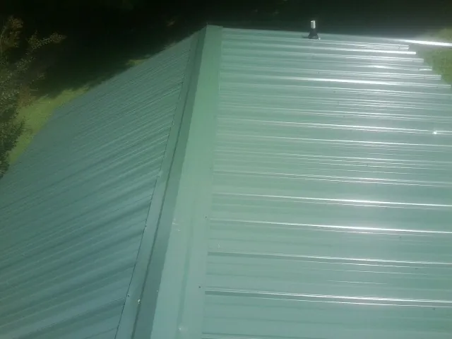 New green metal panels meeting at the ridge of a roof — Flat Roof Repair work by our crew in Shady Cove