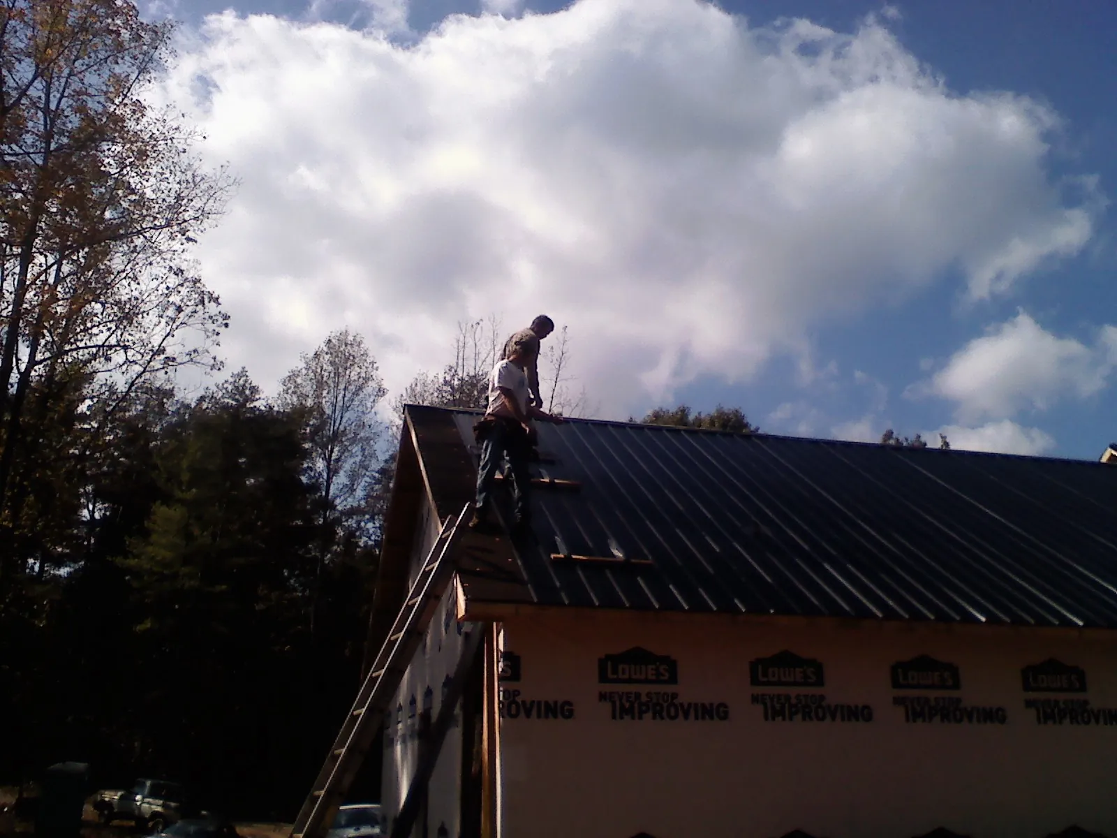 Roofer fastening dark metal panels high against a cloudy sky, from a Roof Inspection job in Shady Cove