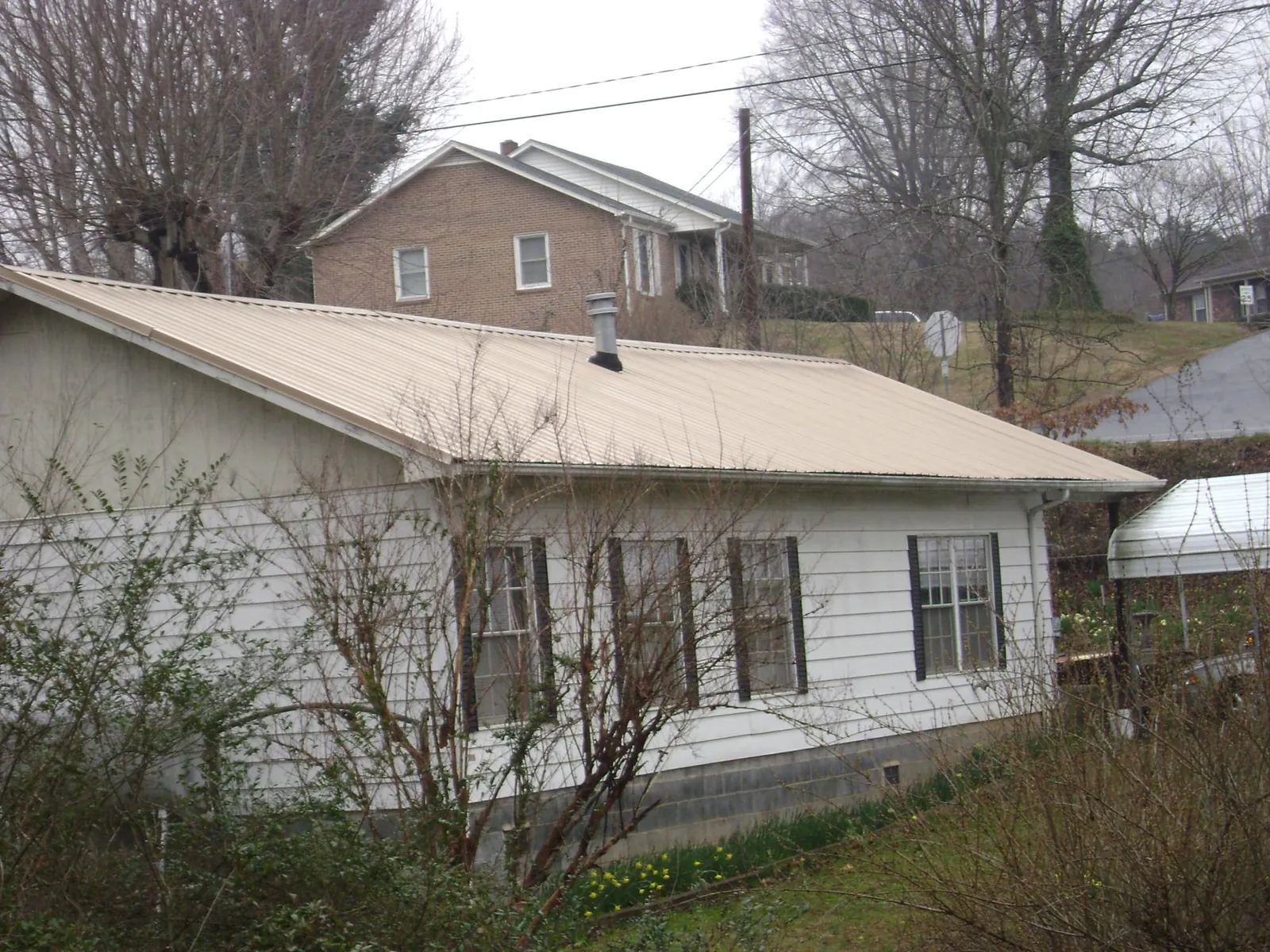 Tan metal roof on a white sided house set into a hillside — Commercial Roofing by Roofing Brothers in Shady Cove