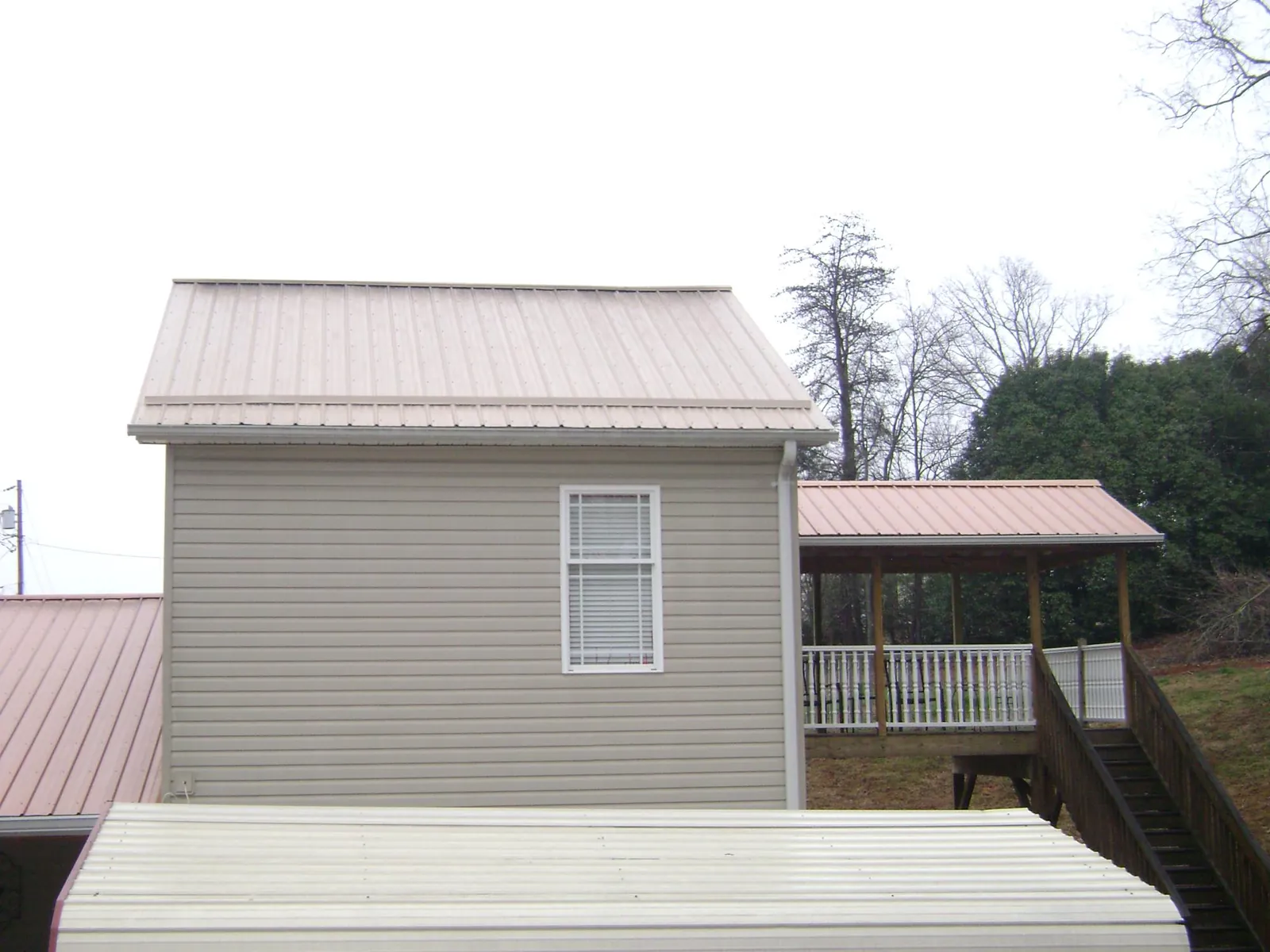 Tan metal roofs on a two story addition and attached porch, from a Roof Replacement job in Shady Cove